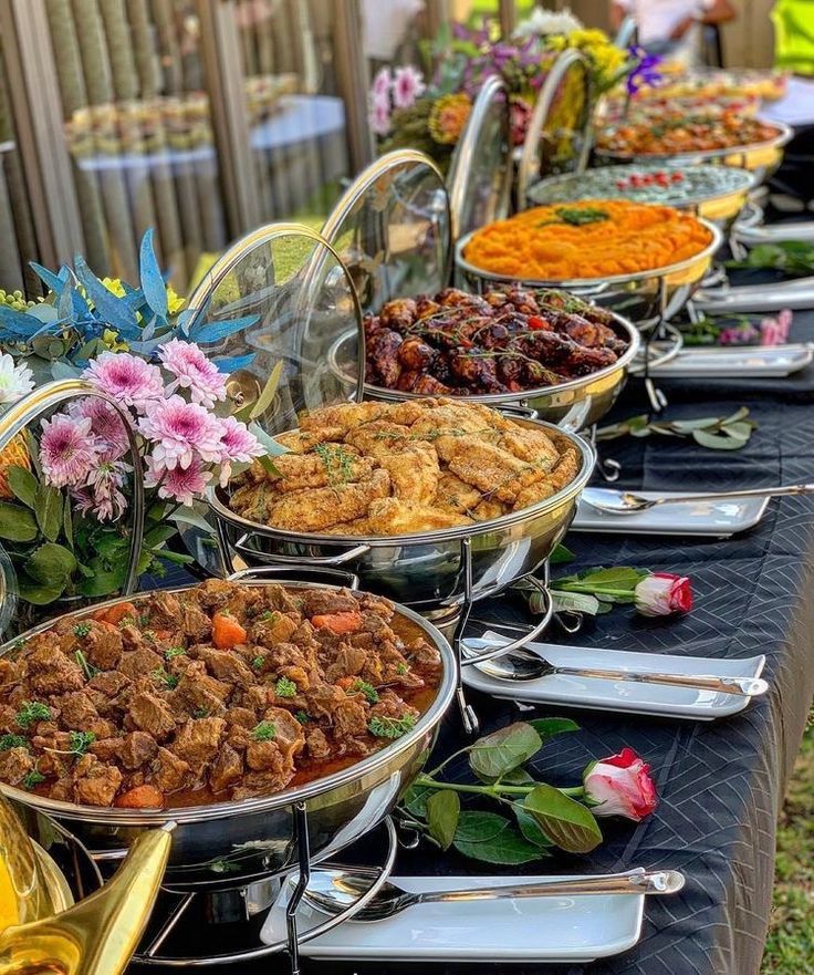 Buffet en extérieur : plats chauds sur des réchauds, fleurs et roses posées sur une nappe noire