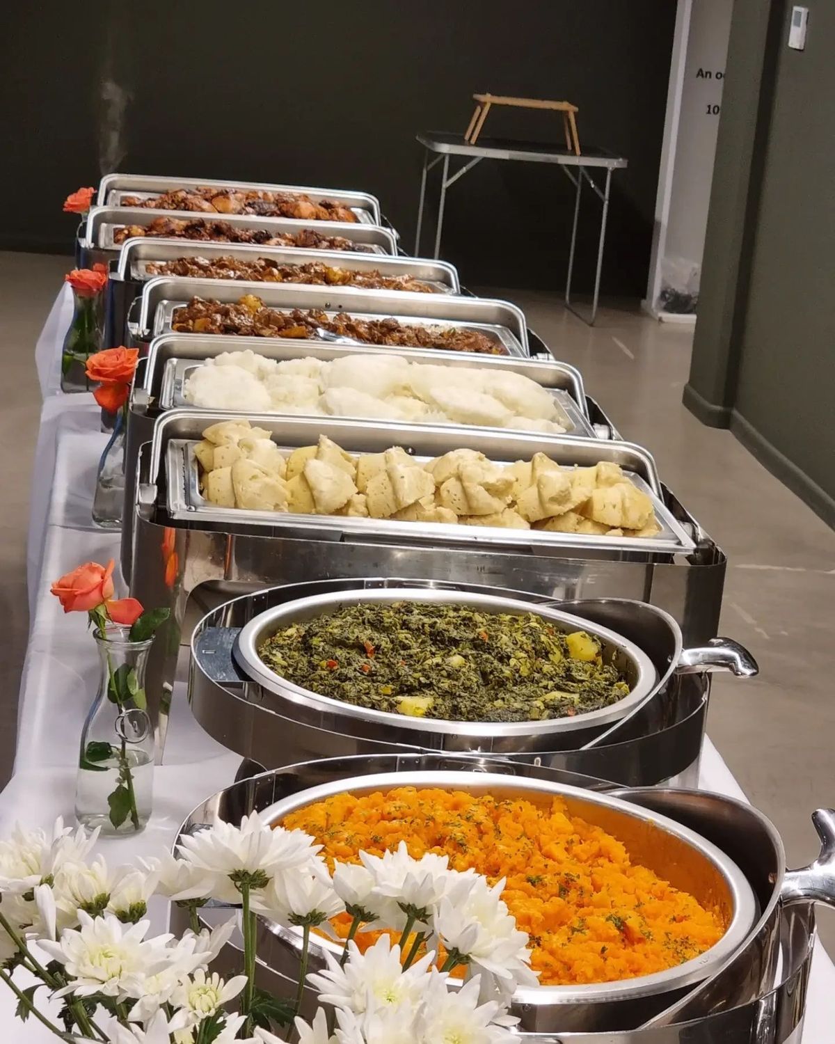 Buffet de plats chauds dans des chauffe-plats en inox, avec des fleurs orange et blanches