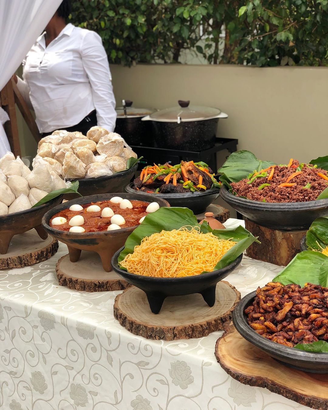 Buffet de plats servis dans des bols en terre cuite posés sur des rondins, sur des feuilles