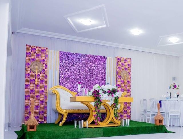Salle de réception avec un fauteuil doré, une table fleurie et un fond en tissu violet