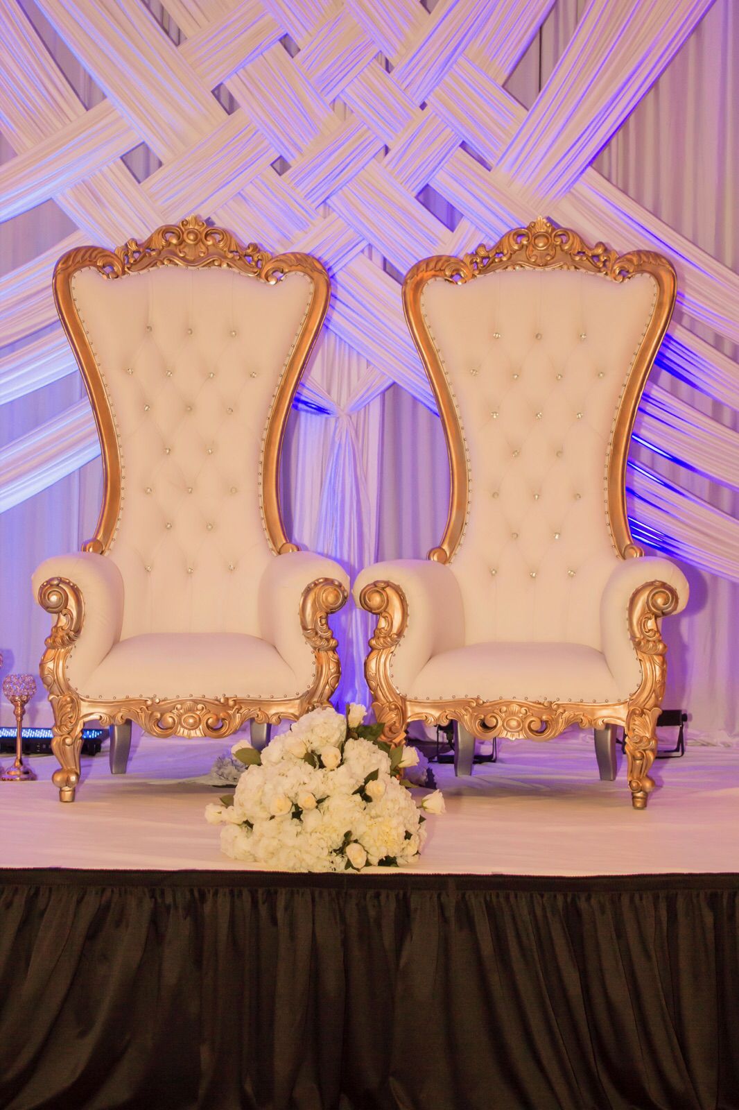 Deux grands fauteuils blancs à cadre doré sculpté, devant un décor de voiles blancs éclairé en violet